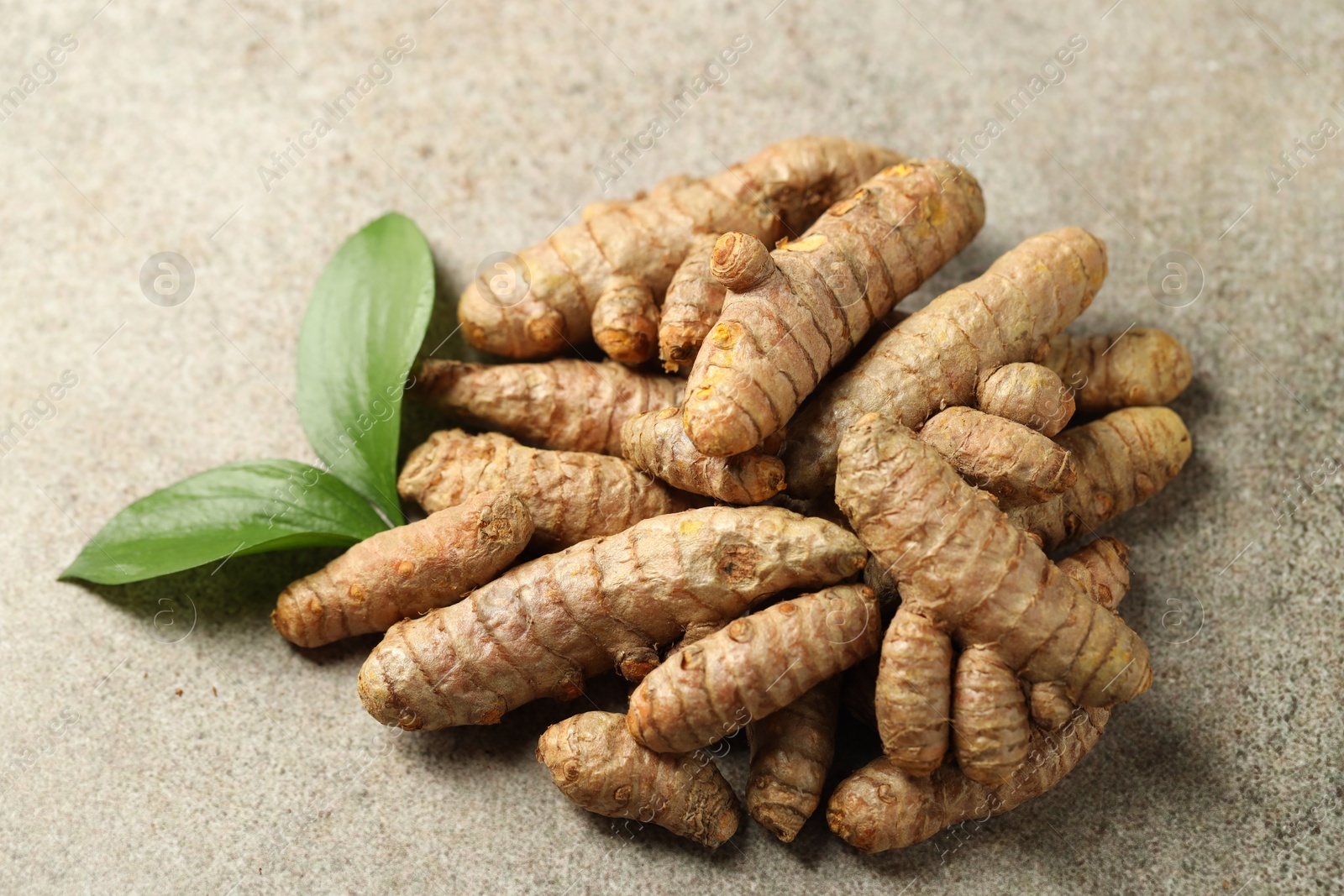 Photo of Pile of tumeric rhizomes with leaves on grey table, closeup