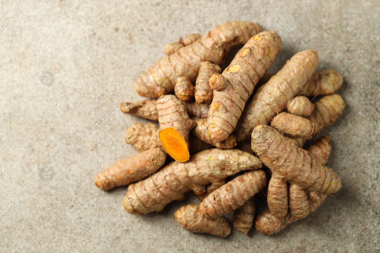 Photo of Pile of tumeric rhizomes on grey table, top view. Space for text