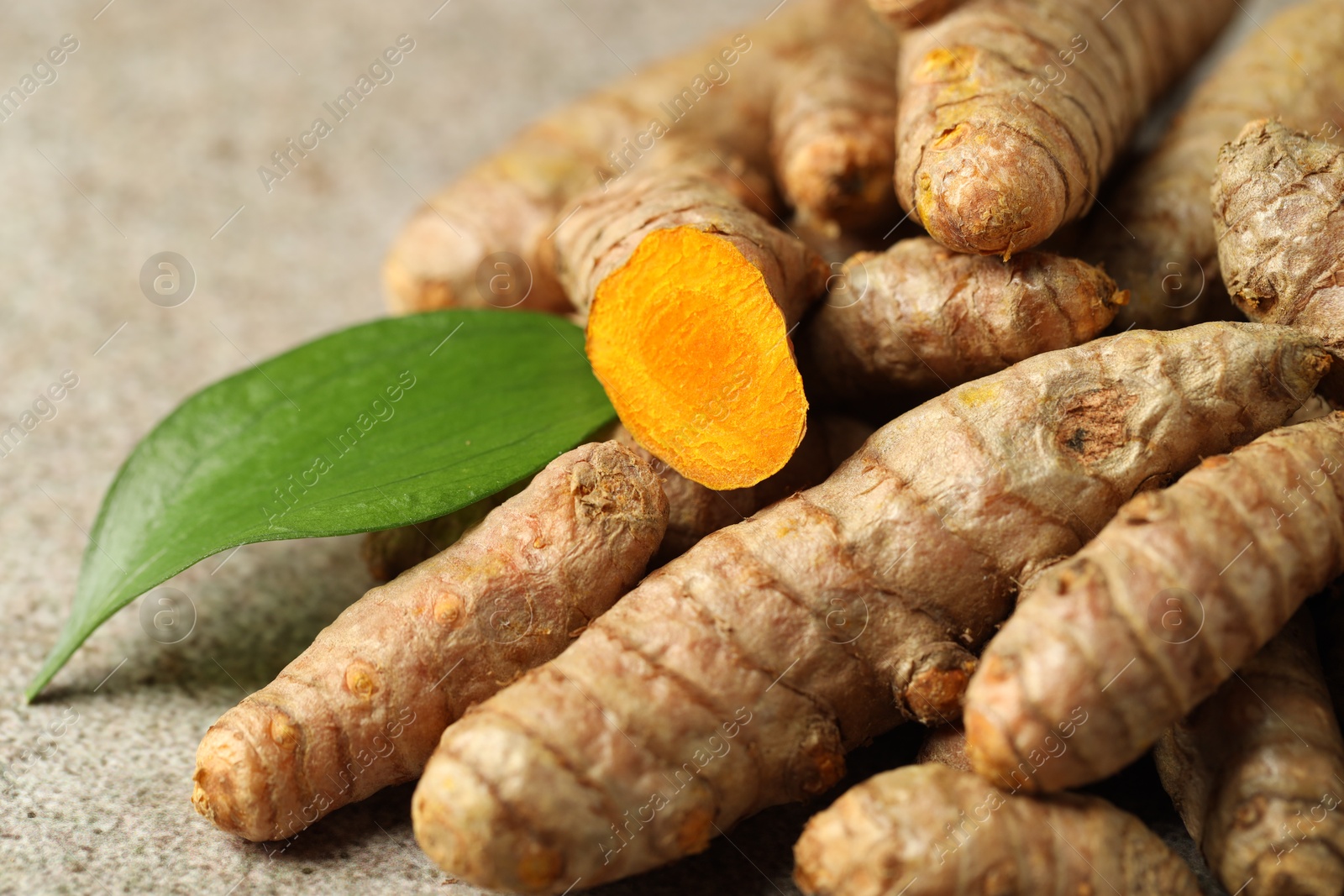 Photo of Pile of tumeric rhizomes with leaf on grey table, closeup