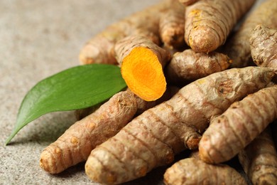 Photo of Pile of tumeric rhizomes with leaf on grey table, closeup