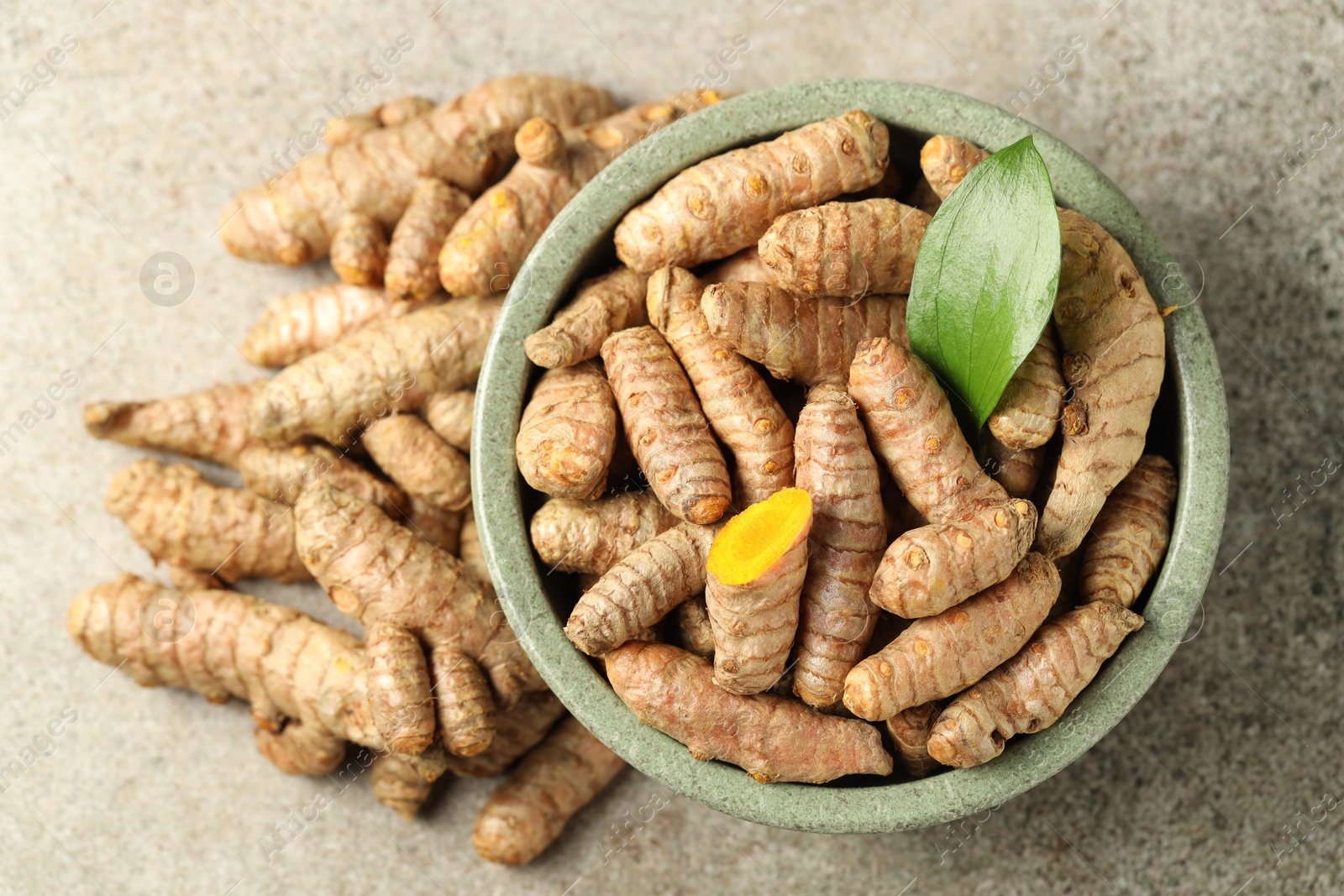 Photo of Tumeric rhizomes with leaf in bowl on grey table, top view