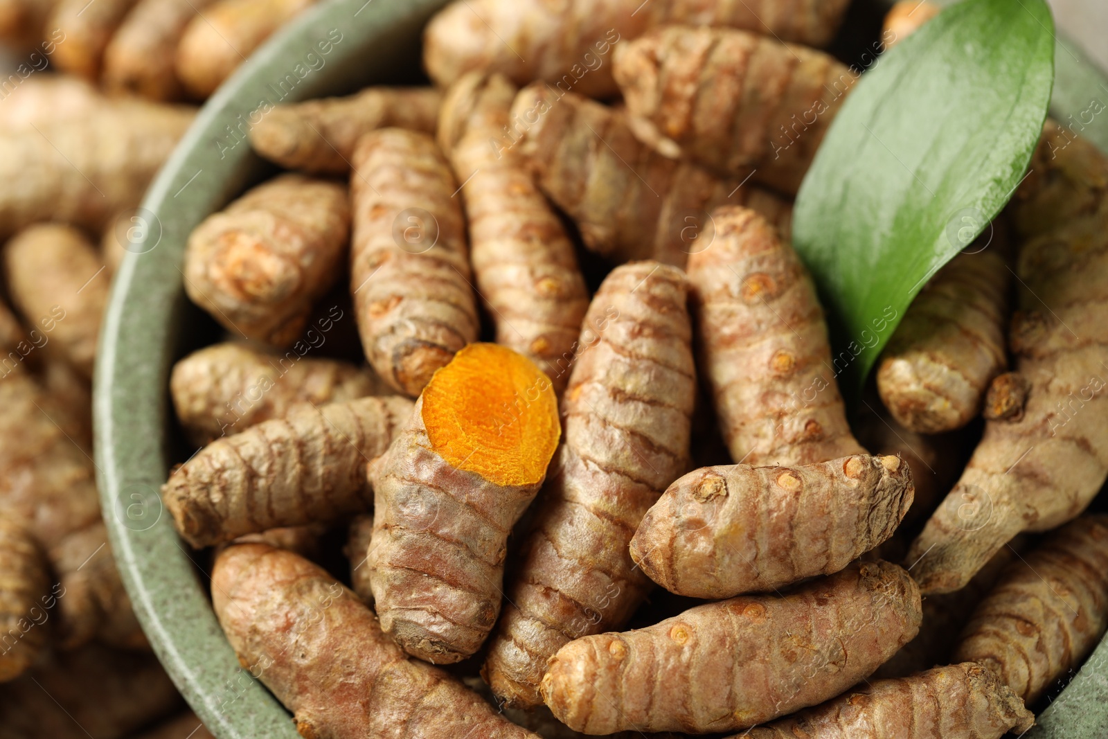 Photo of Tumeric rhizomes with leaf in bowl on table, closeup