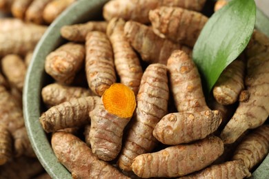 Photo of Tumeric rhizomes with leaf in bowl on table, closeup