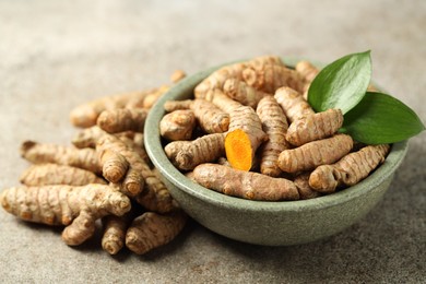 Photo of Tumeric rhizomes with leaves in bowl on grey table, closeup