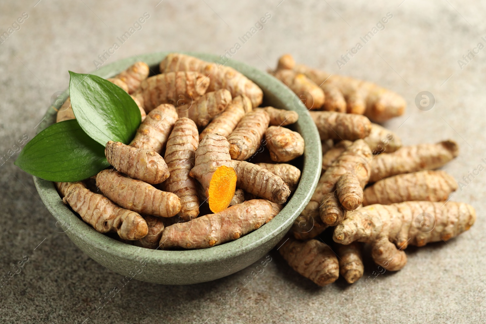 Photo of Tumeric rhizomes with leaves in bowl on grey table, closeup