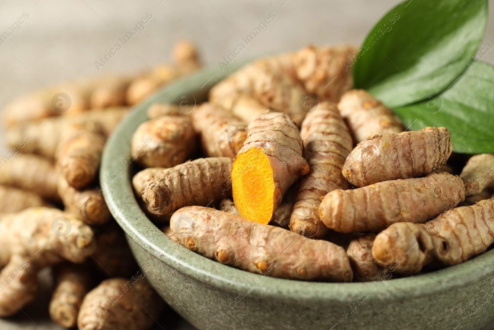 Photo of Tumeric rhizomes with leaves in bowl on grey table, closeup