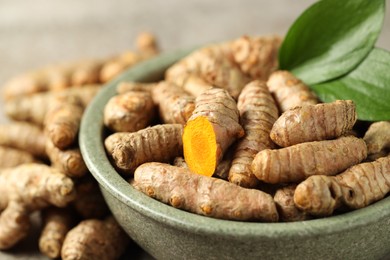 Photo of Tumeric rhizomes with leaves in bowl on grey table, closeup