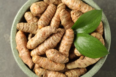 Photo of Tumeric rhizomes with leaves in bowl on grey table, top view