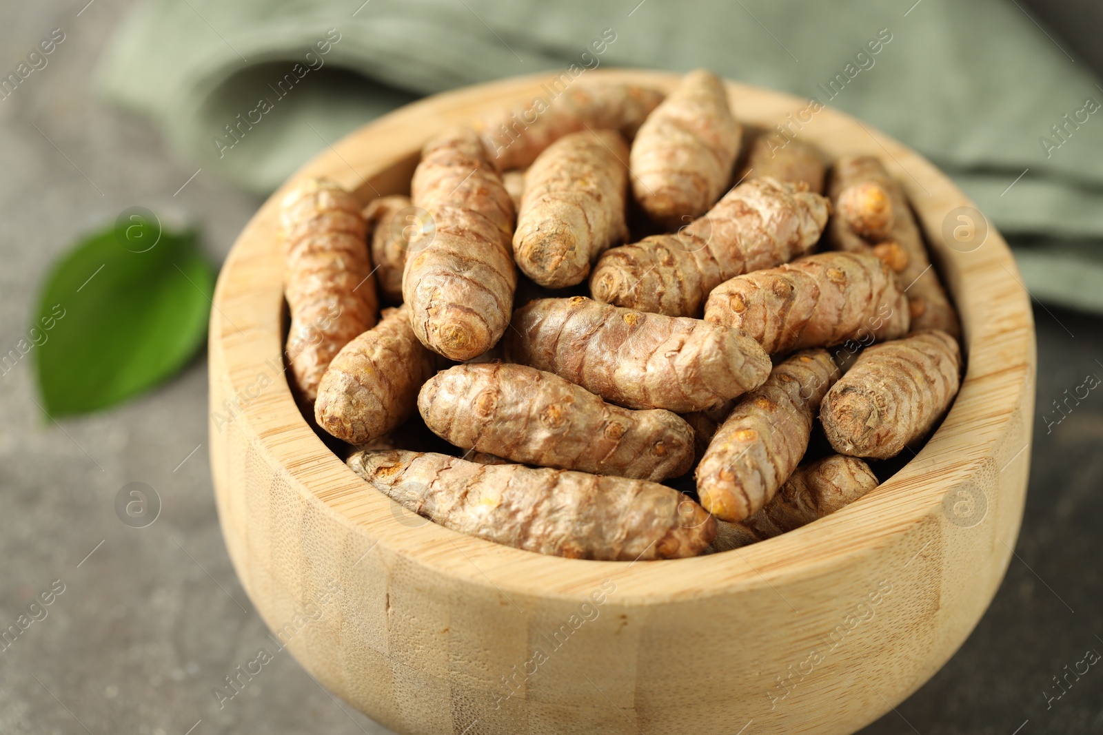 Photo of Tumeric rhizomes in bowl on grey table, closeup