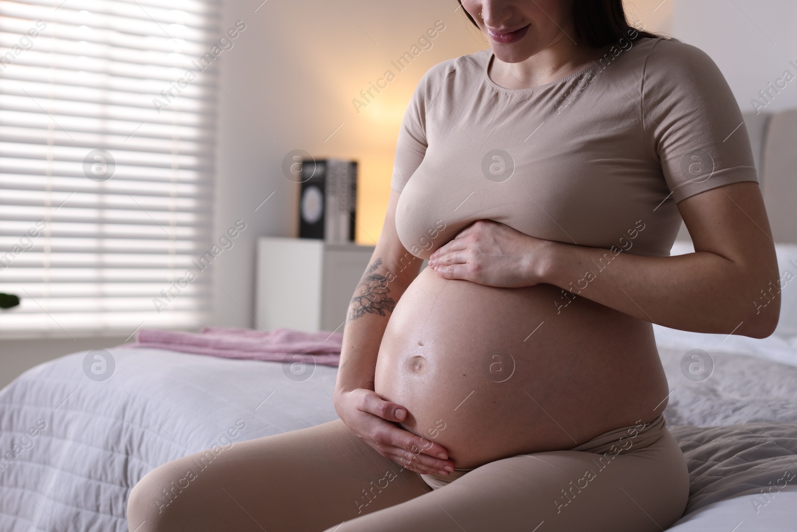 Photo of Pregnant woman with cute belly on bed at home, closeup