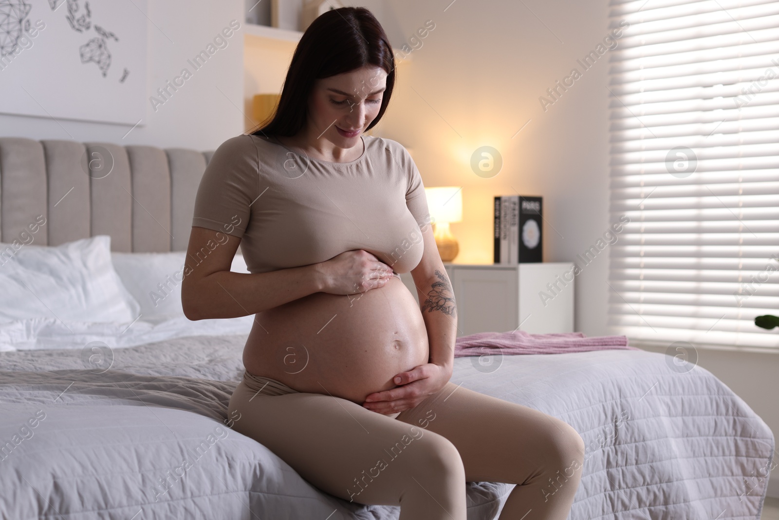 Photo of Beautiful pregnant woman with cute belly on bed at home