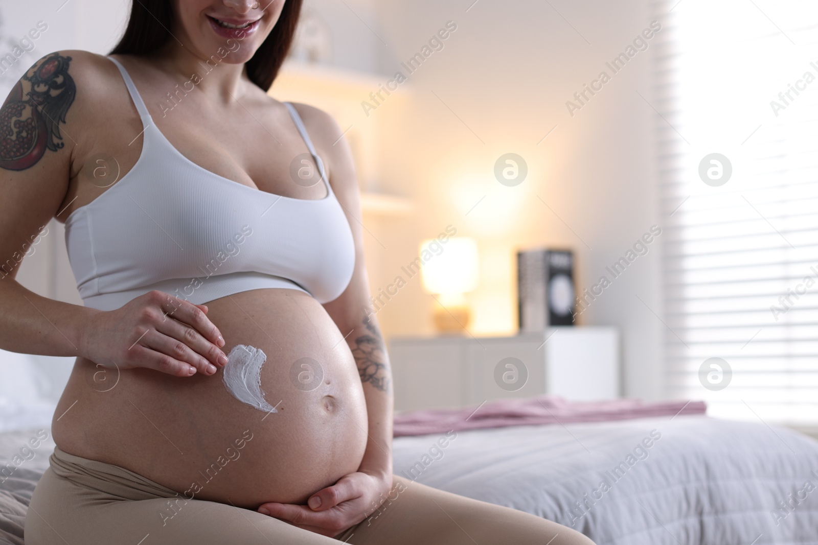 Photo of Pregnant woman applying cream on belly at home, closeup. Space for text