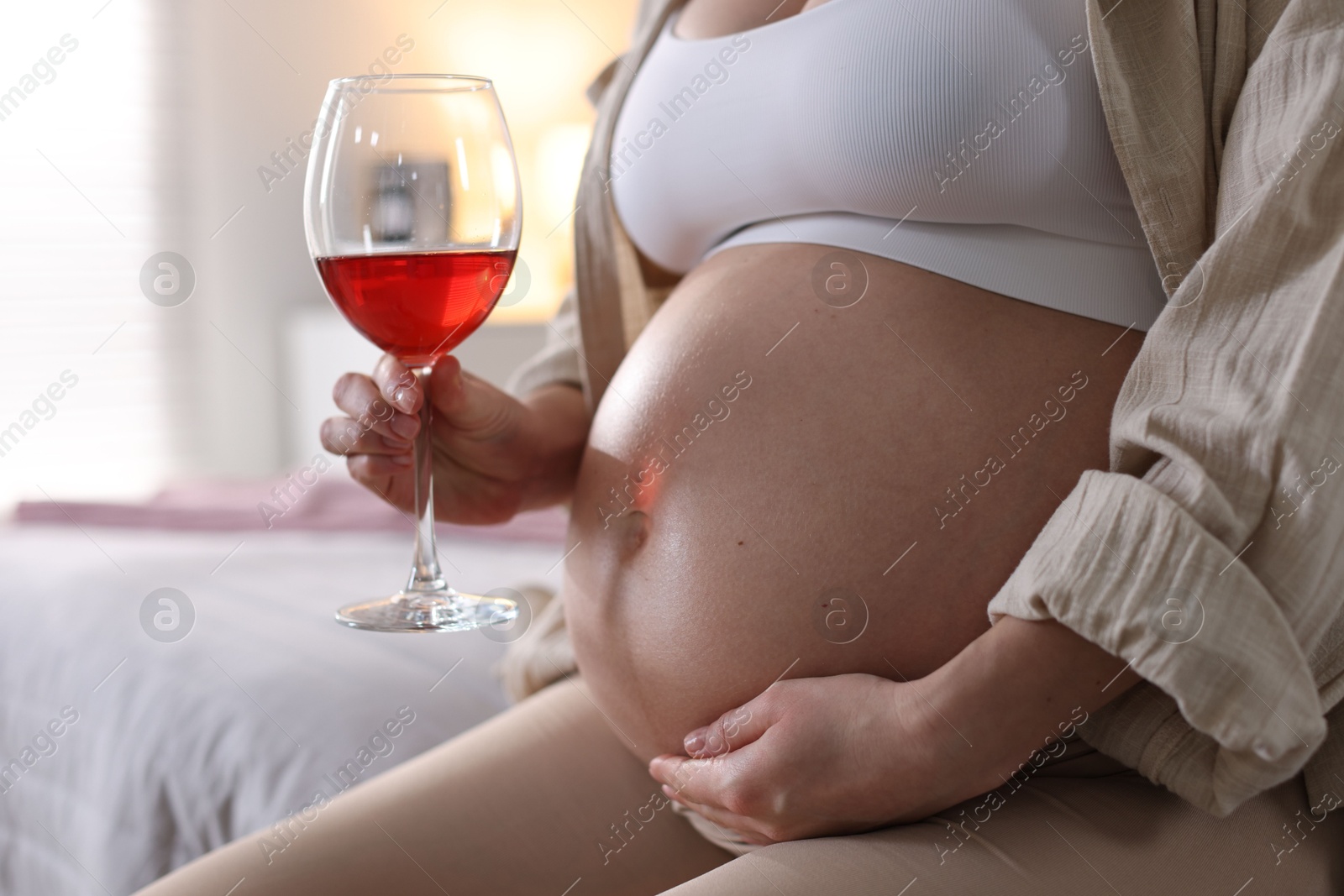 Photo of Pregnant woman with glass of red wine at home, closeup