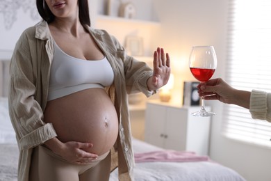 Photo of Pregnant woman refusing glass of red wine at home, closeup