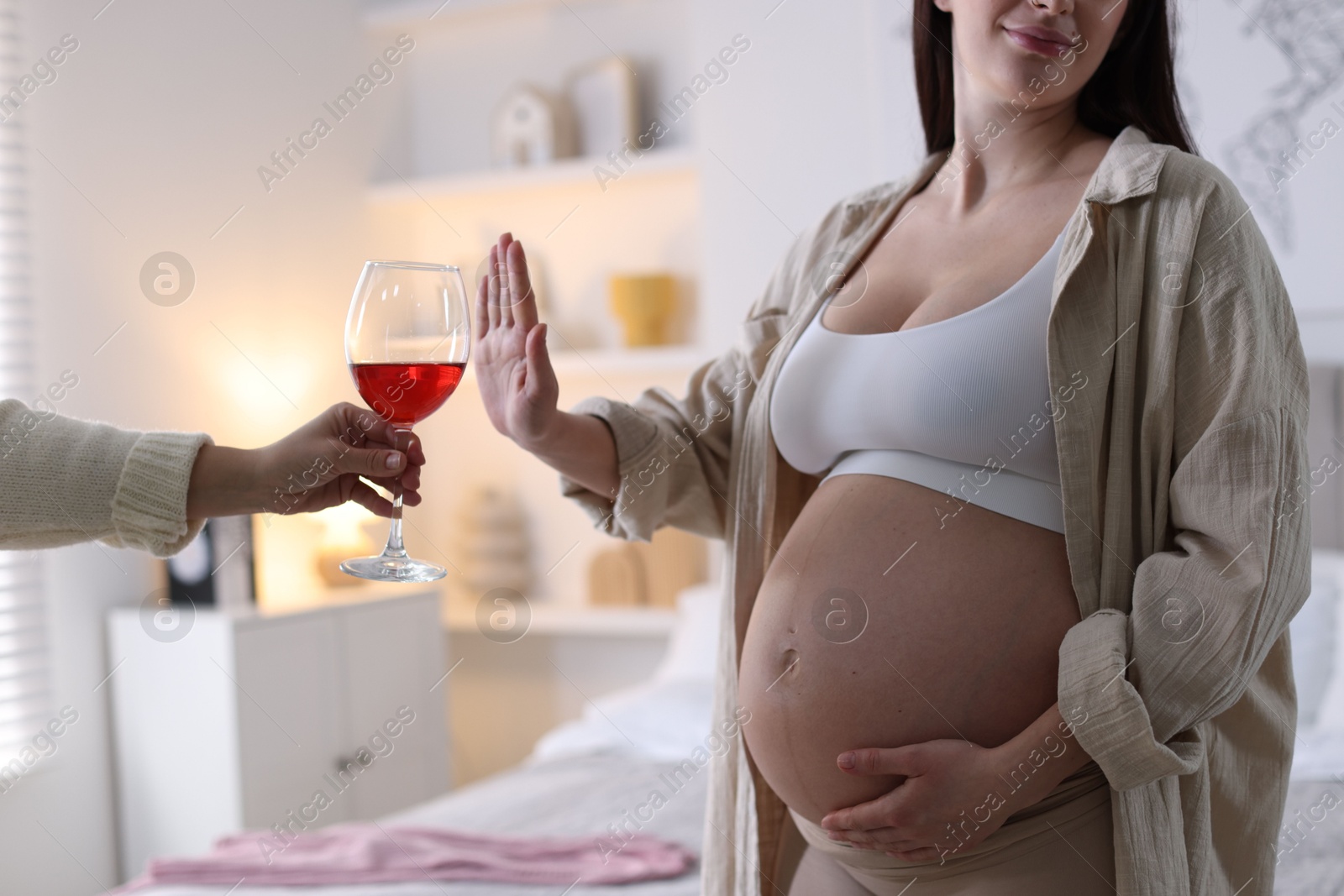 Photo of Pregnant woman refusing glass of red wine at home, closeup