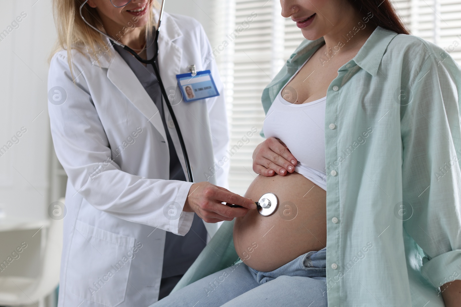 Photo of Pregnancy checkup. Doctor with stethoscope listening baby's heartbeat in patient's tummy indoors, closeup