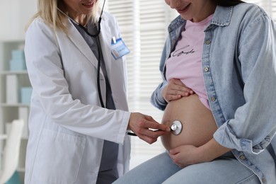 Photo of Pregnancy checkup. Doctor with stethoscope listening baby's heartbeat in patient's tummy indoors, closeup