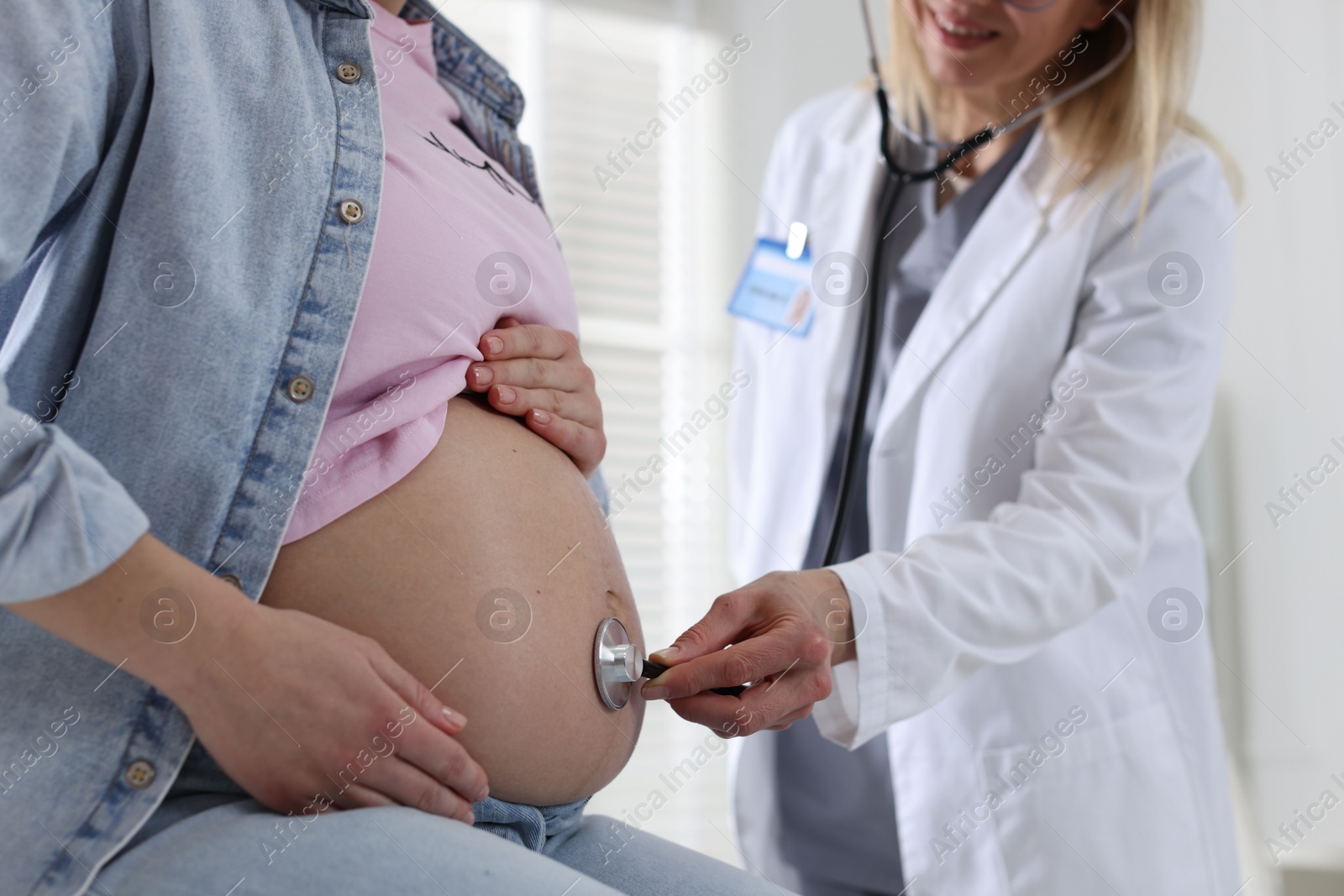 Photo of Pregnancy checkup. Doctor with stethoscope listening baby's heartbeat in patient's tummy indoors, closeup