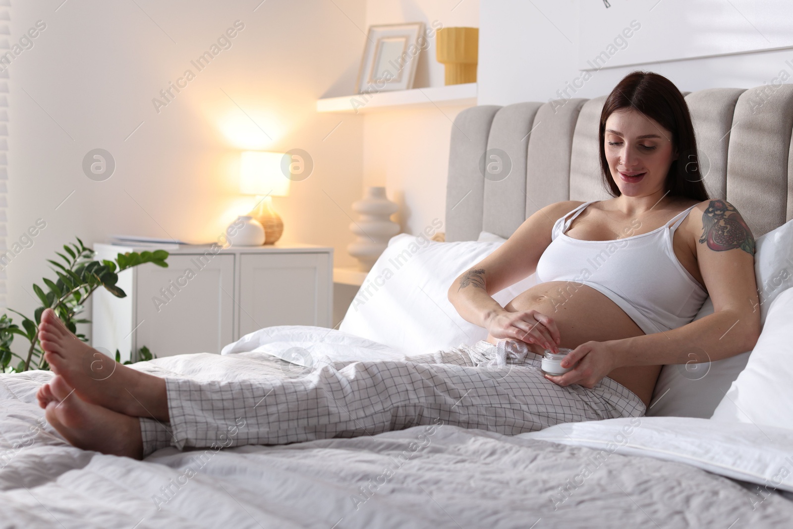 Photo of Pregnant woman with jar of cream on bed at home