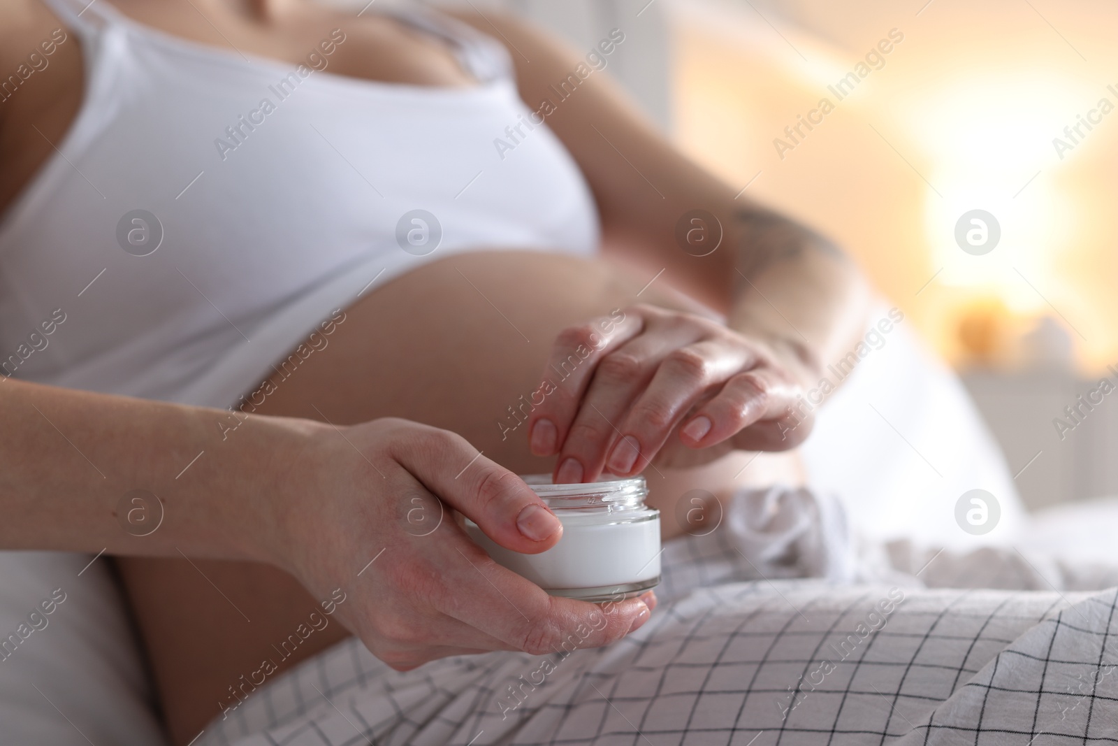 Photo of Pregnant woman with jar of cream at home, closeup