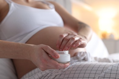 Photo of Pregnant woman with jar of cream at home, closeup