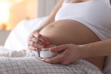 Photo of Pregnant woman with jar of cream at home, closeup