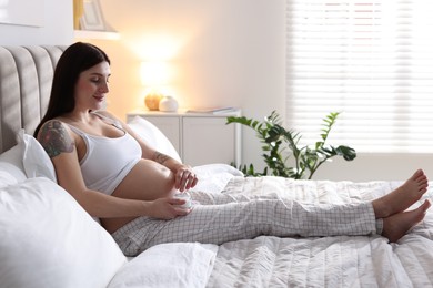 Photo of Pregnant woman with jar of cream on bed at home