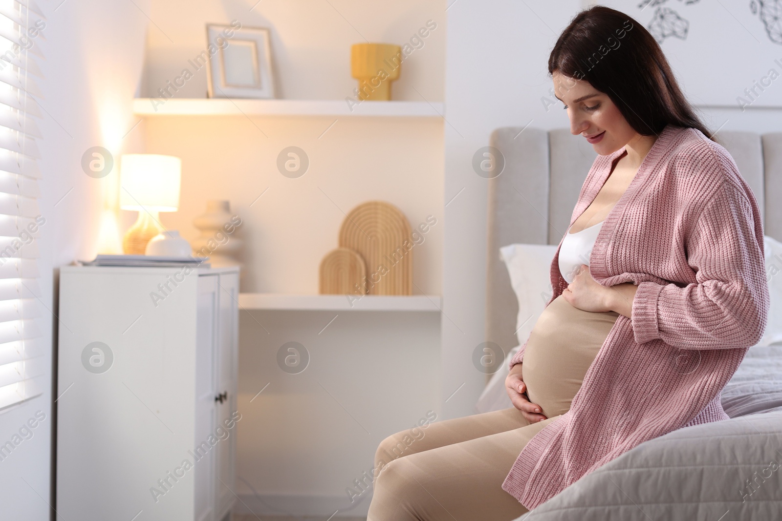 Photo of Beautiful pregnant woman with cute belly on bed at home, space for text