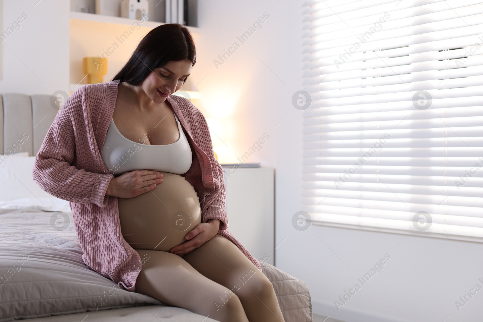 Photo of Beautiful pregnant woman with cute belly on bed at home, space for text