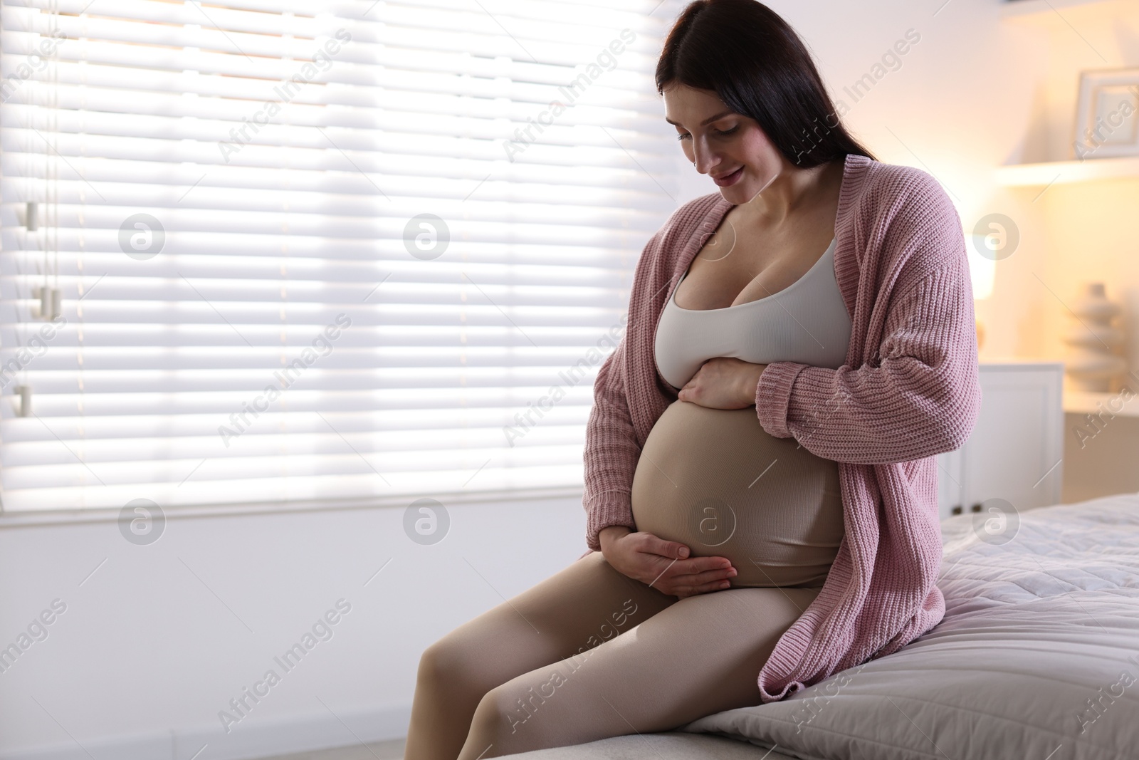 Photo of Beautiful pregnant woman with cute belly on bed at home, space for text