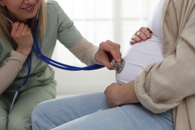 Photo of Pregnancy checkup. Doctor with stethoscope listening baby's heartbeat in patient's tummy indoors, closeup