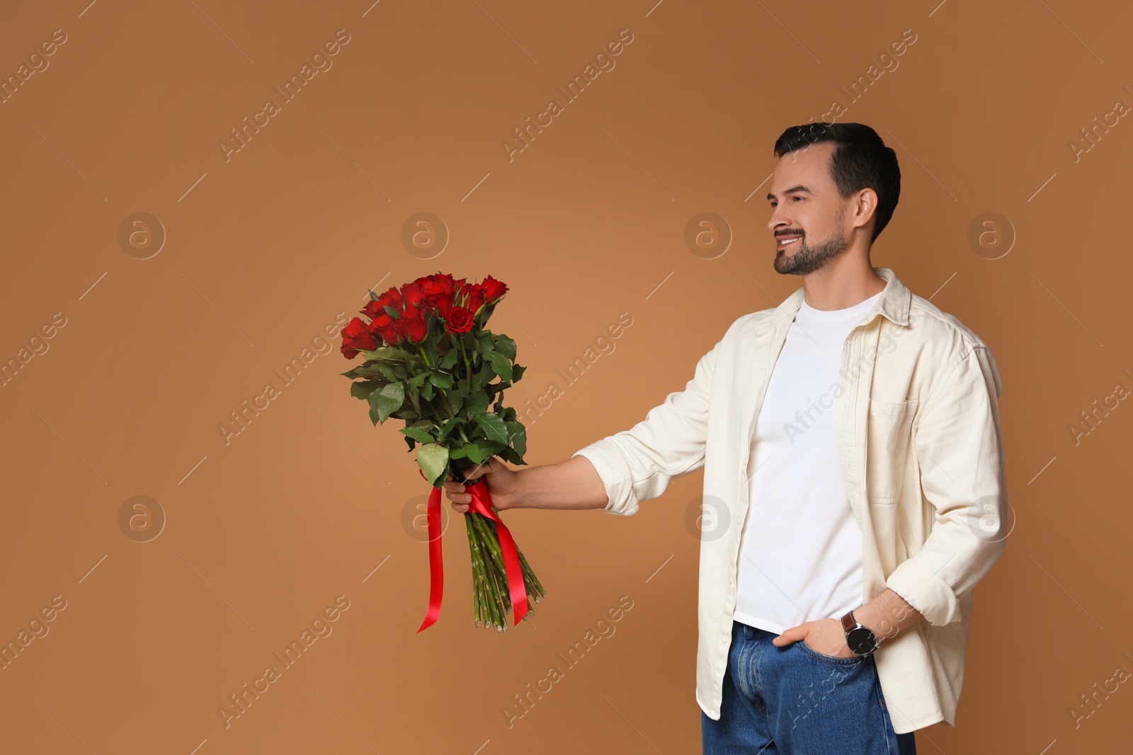 Photo of Happy Valentine's Day. Handsome man with bouquet of roses on brown background