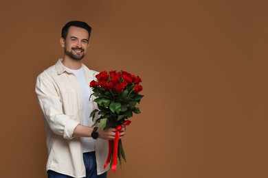 Photo of Happy Valentine's Day. Handsome man with bouquet of roses on brown background. Space for text