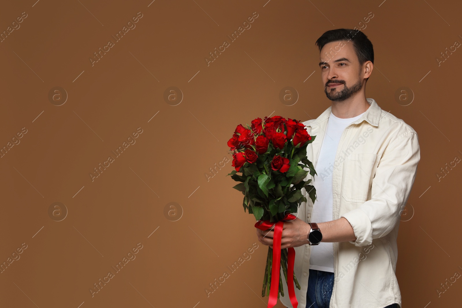 Photo of Happy Valentine's Day. Handsome man with bouquet of roses on brown background. Space for text