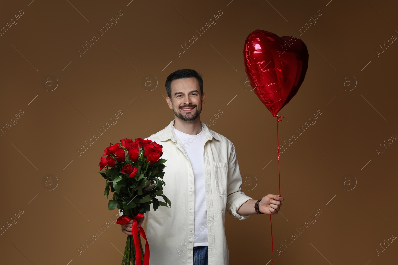 Photo of Happy Valentine's Day. Handsome man with bouquet of roses and heart shaped balloon on brown background