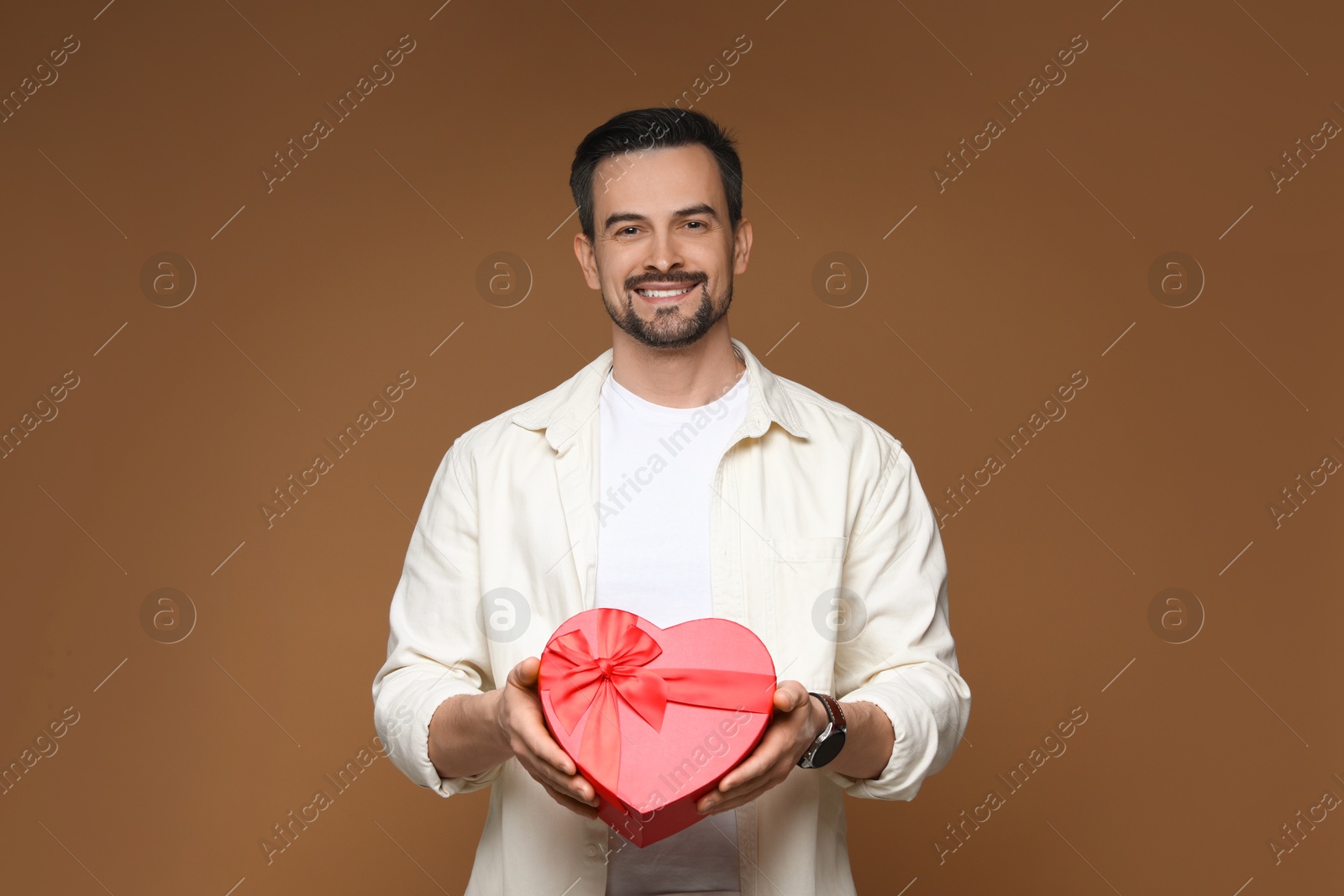 Photo of Happy Valentine's Day. Handsome man with heart shaped gift box on brown background