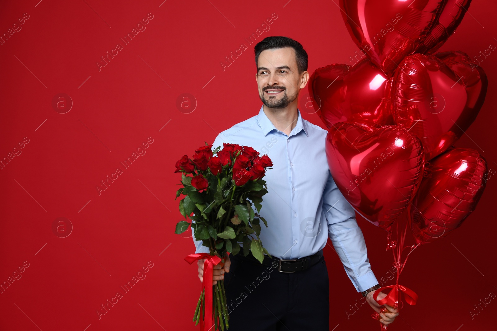 Photo of Happy Valentine's Day. Handsome man with bouquet of roses and heart shaped balloons on red background. Space for text