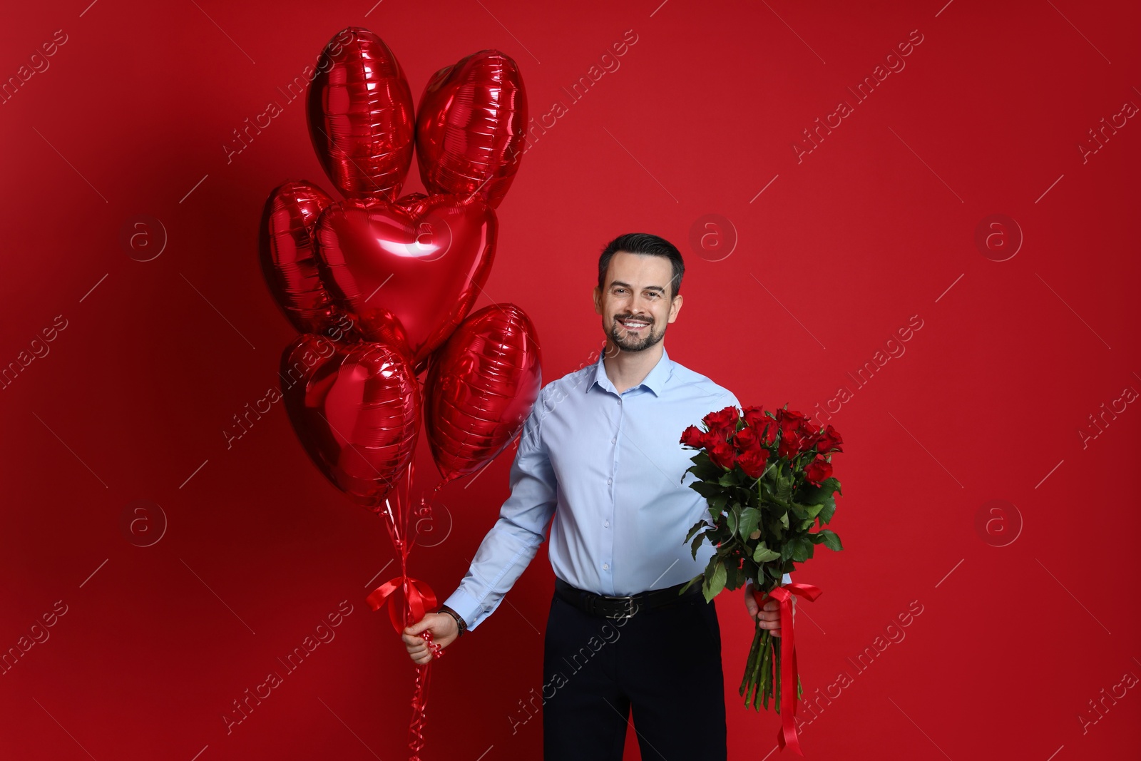 Photo of Happy Valentine's Day. Handsome man with bouquet of roses and heart shaped balloons on red background