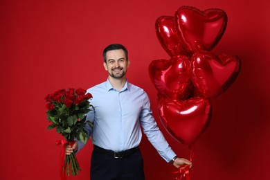 Photo of Happy Valentine's Day. Handsome man with bouquet of roses and heart shaped balloons on red background