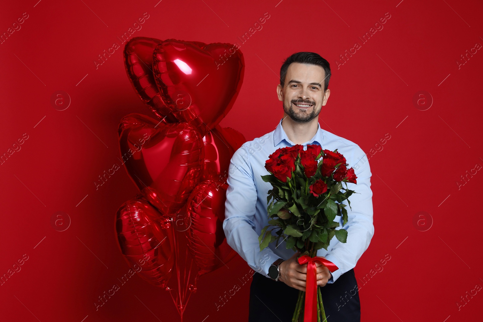 Photo of Happy Valentine's Day. Handsome man with bouquet of roses and heart shaped balloons on red background