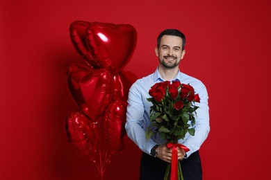 Photo of Happy Valentine's Day. Handsome man with bouquet of roses and heart shaped balloons on red background