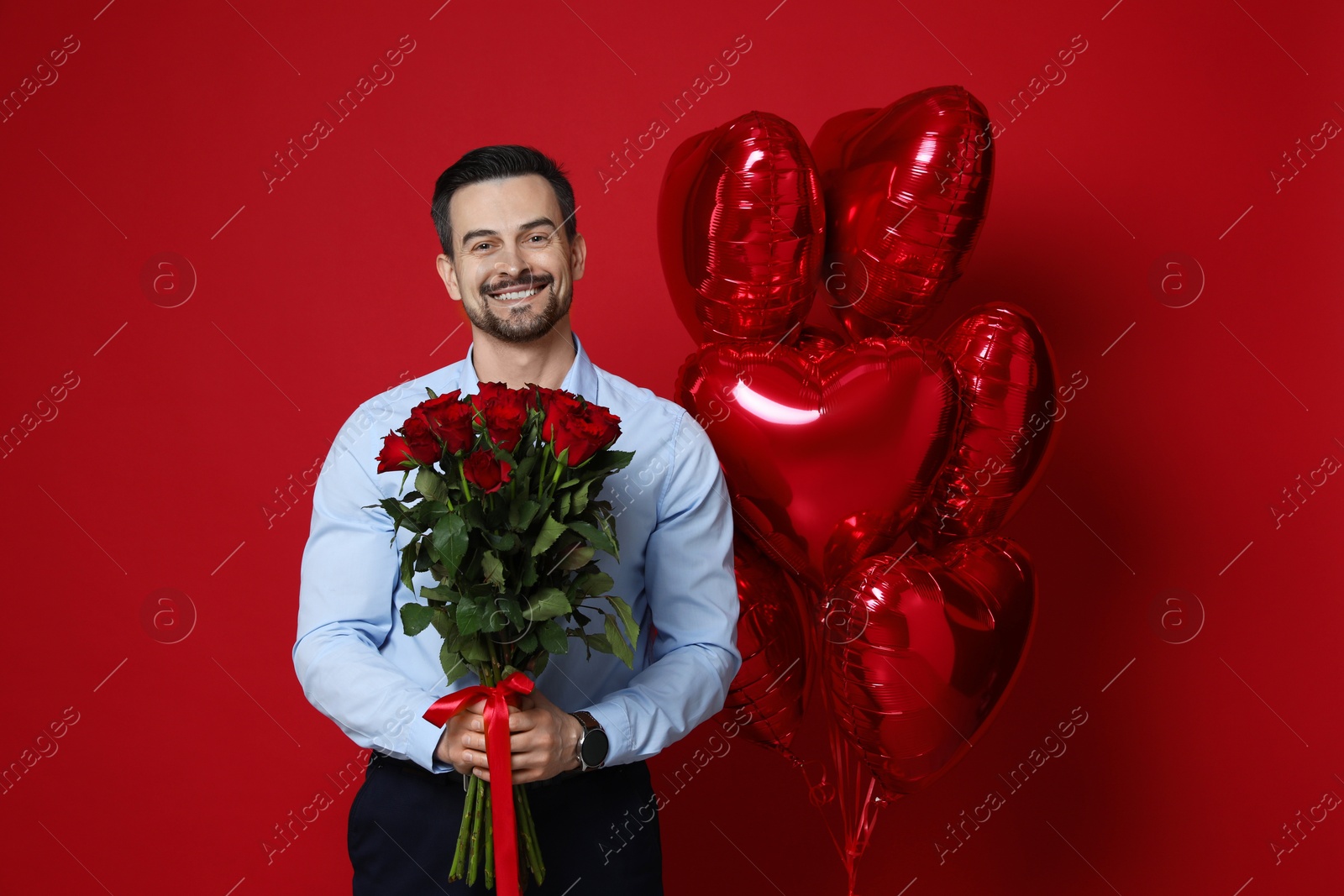 Photo of Happy Valentine's Day. Handsome man with bouquet of roses and heart shaped balloons on red background