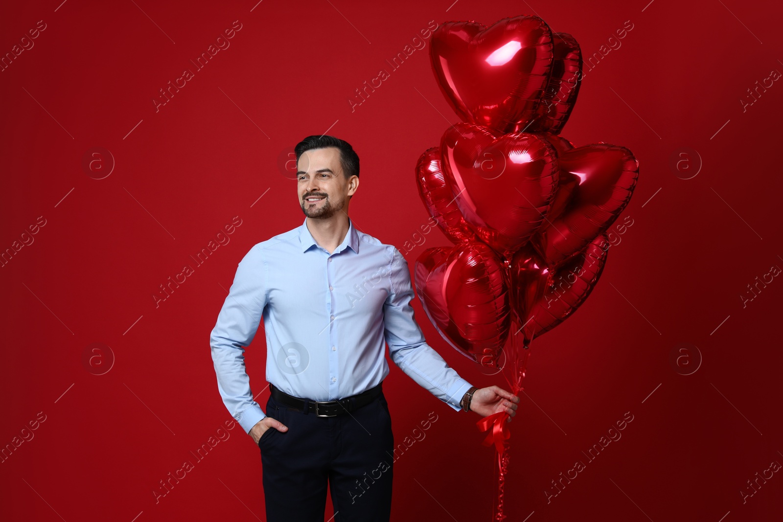 Photo of Happy Valentine's Day. Handsome man with heart shaped balloons on red background