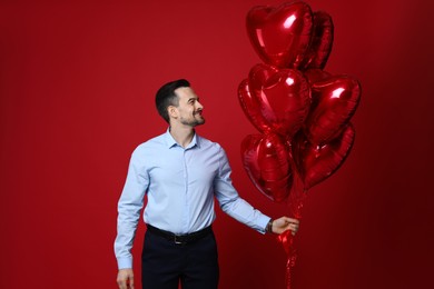 Photo of Happy Valentine's Day. Handsome man with heart shaped balloons on red background