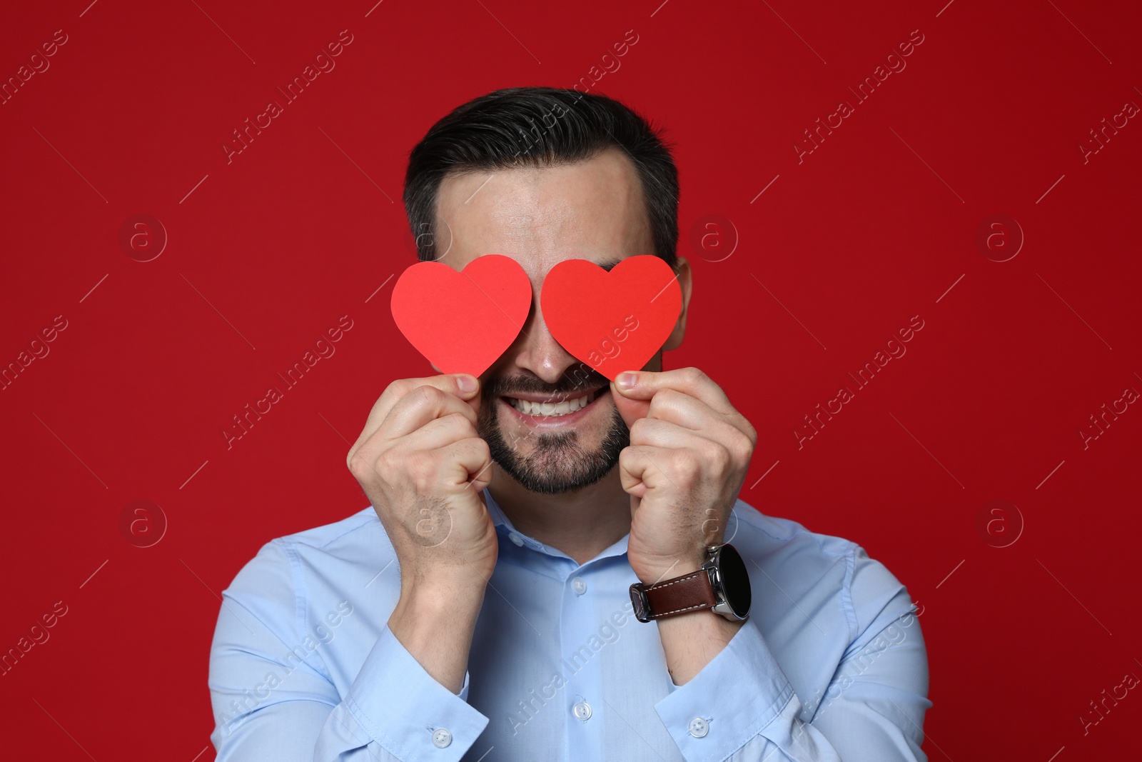 Photo of Happy Valentine's Day. Man covering his face with paper hearts on red background