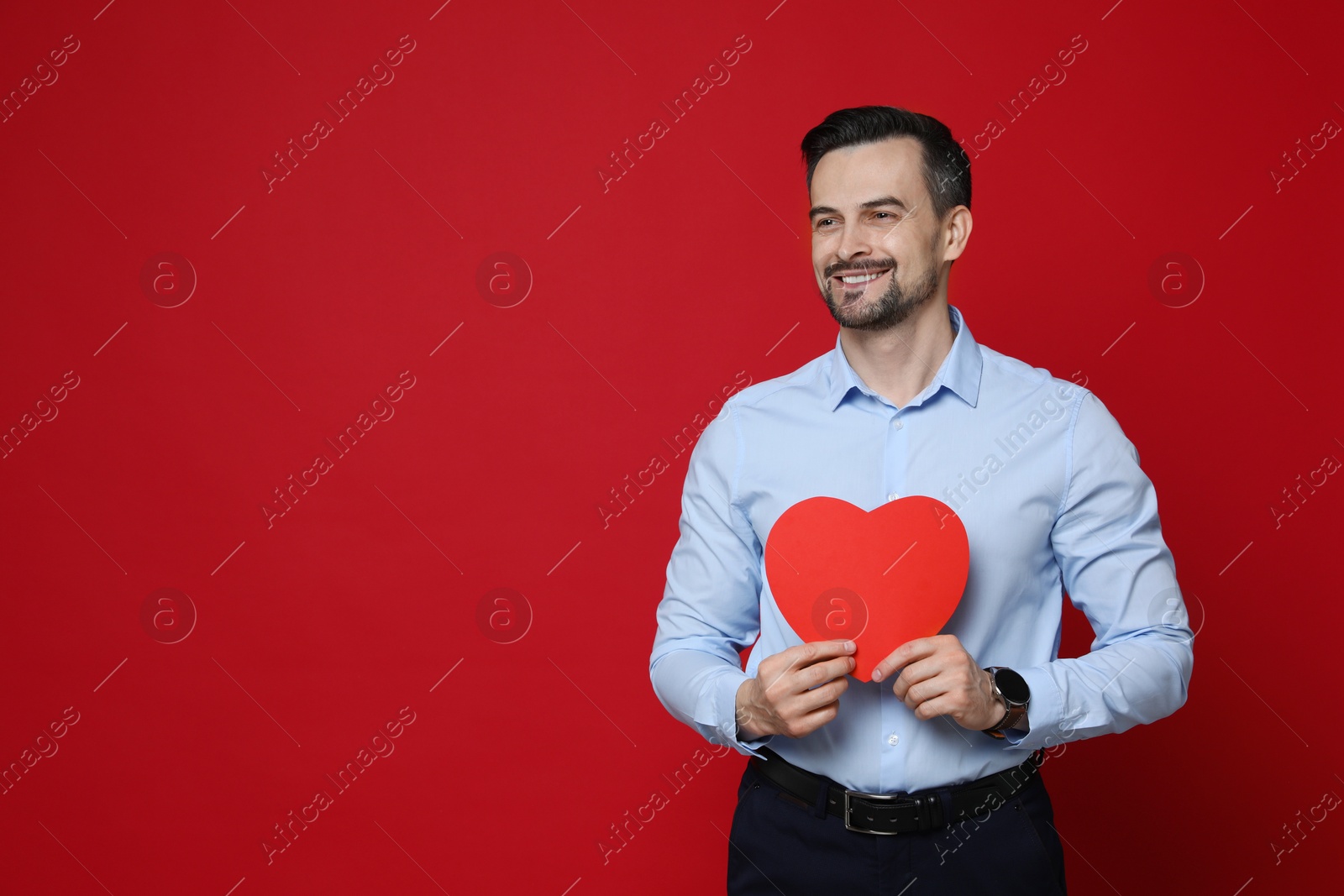 Photo of Happy Valentine's Day. Handsome man with paper heart on red background. Space for text