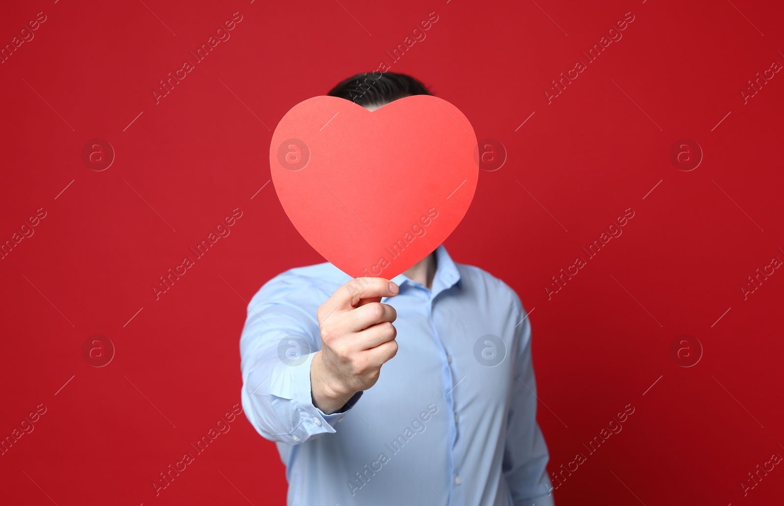 Photo of Happy Valentine's Day. Man covering his face with paper heart on red background