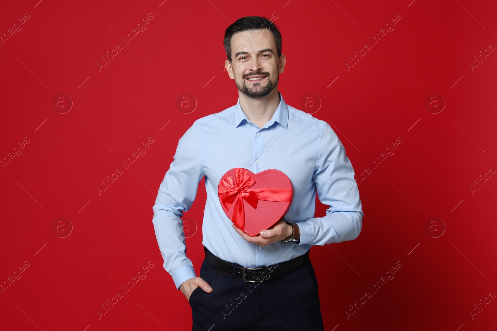 Photo of Happy Valentine's Day. Handsome man with heart shaped gift box on red background