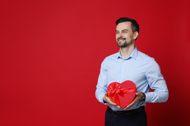 Photo of Happy Valentine's Day. Handsome man with heart shaped gift box on red background. Space for text