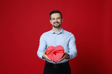 Photo of Happy Valentine's Day. Handsome man with heart shaped gift box on red background